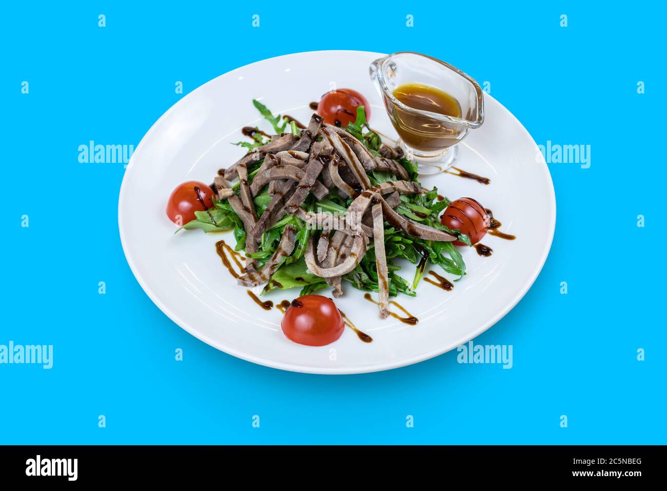 Salade d'arugula avec langue de boeuf et sauce miel-moutarde isolée sur le bleu Banque D'Images