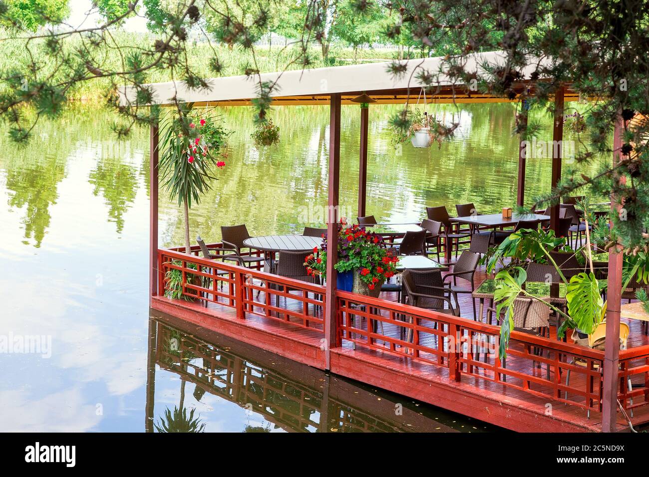 restaurant flottant sur un quai rouge avec une voûte sur des tables avec des chaises et des pots de fleurs sur les rives de la rivière, en été. Banque D'Images