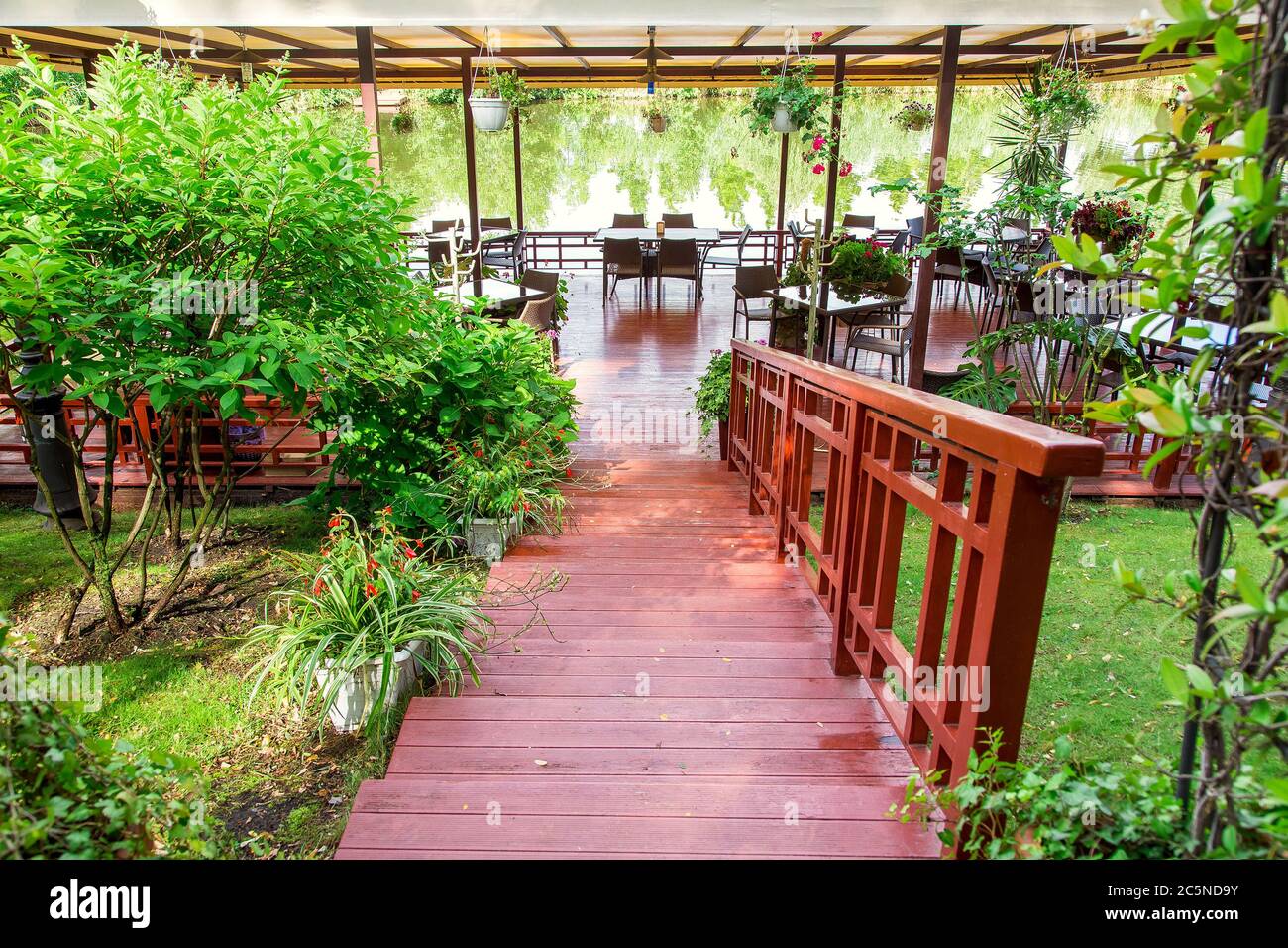 escalier en bois avec une rampe sur la pente jusqu'à la jetée avec une verrière jusqu'à un restaurant flottant avec des tables au bord de l'eau, des plantes et des fleurs en f Banque D'Images