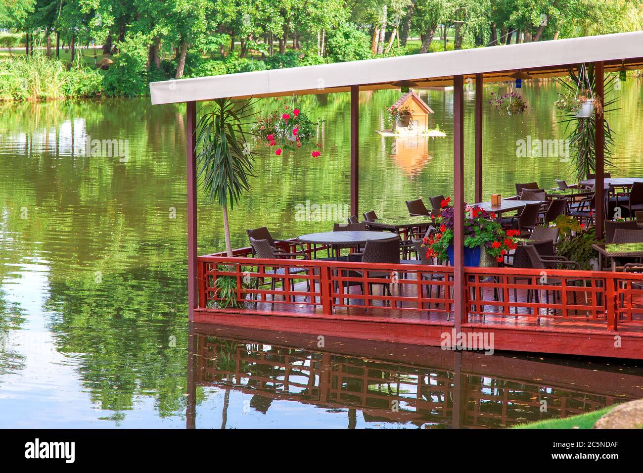 restaurant flottant sur un quai rouge avec une voûte sur des tables avec des chaises et des pots de fleurs sur les rives de la rivière avec des arbres verts par jour d'été. Banque D'Images