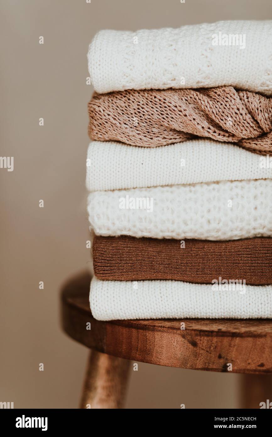 Composition de mode pour femmes. Chaud hiver femme wollen tricoté chandails, pullovers s'empilent sur un tabouret en bois sur fond blanc. Concept de vêtements modernes Banque D'Images