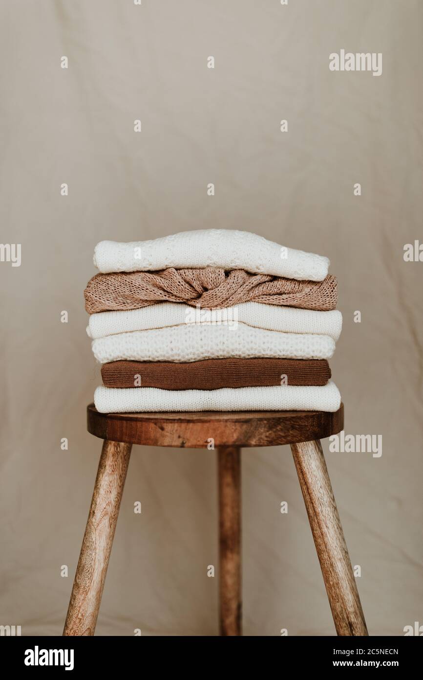 Composition de mode pour femmes. Chaud hiver femme wollen tricoté chandails, pullovers s'empilent sur un tabouret en bois sur fond blanc. Concept de vêtements modernes Banque D'Images