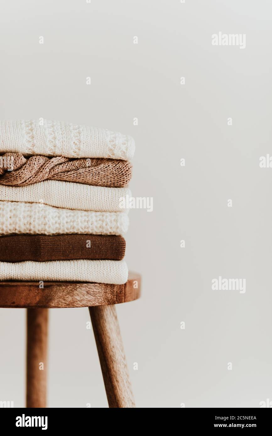 Composition de mode pour femmes. Chaud hiver femme wollen tricoté chandails, pullovers s'empilent sur un tabouret en bois sur fond blanc. Concept de vêtements modernes Banque D'Images