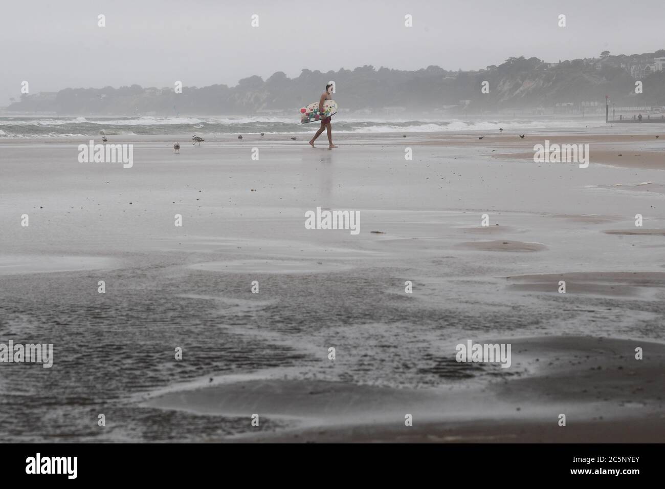 Surfeur sur la plage de Bournemouth malgré la pluie et la bruine que l'on attend dans une grande partie du pays. Banque D'Images