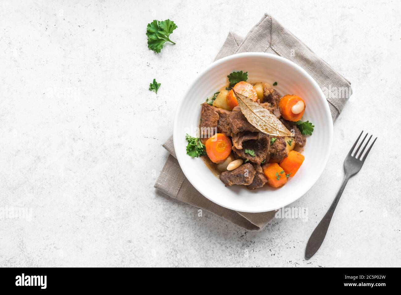 Viande de bœuf compotée de pommes de terre, carottes et épices sur fond blanc, vue du dessus. Plats maison de confort d'hiver - ragoût de viande lentement cuit dans un bol. Banque D'Images