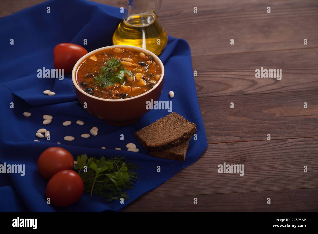 Soupe de légumes et de haricots, tomates, huile dans une bouteille et pain de seigle sur un tissu bleu sur fond de bois. Une alimentation saine. Banque D'Images