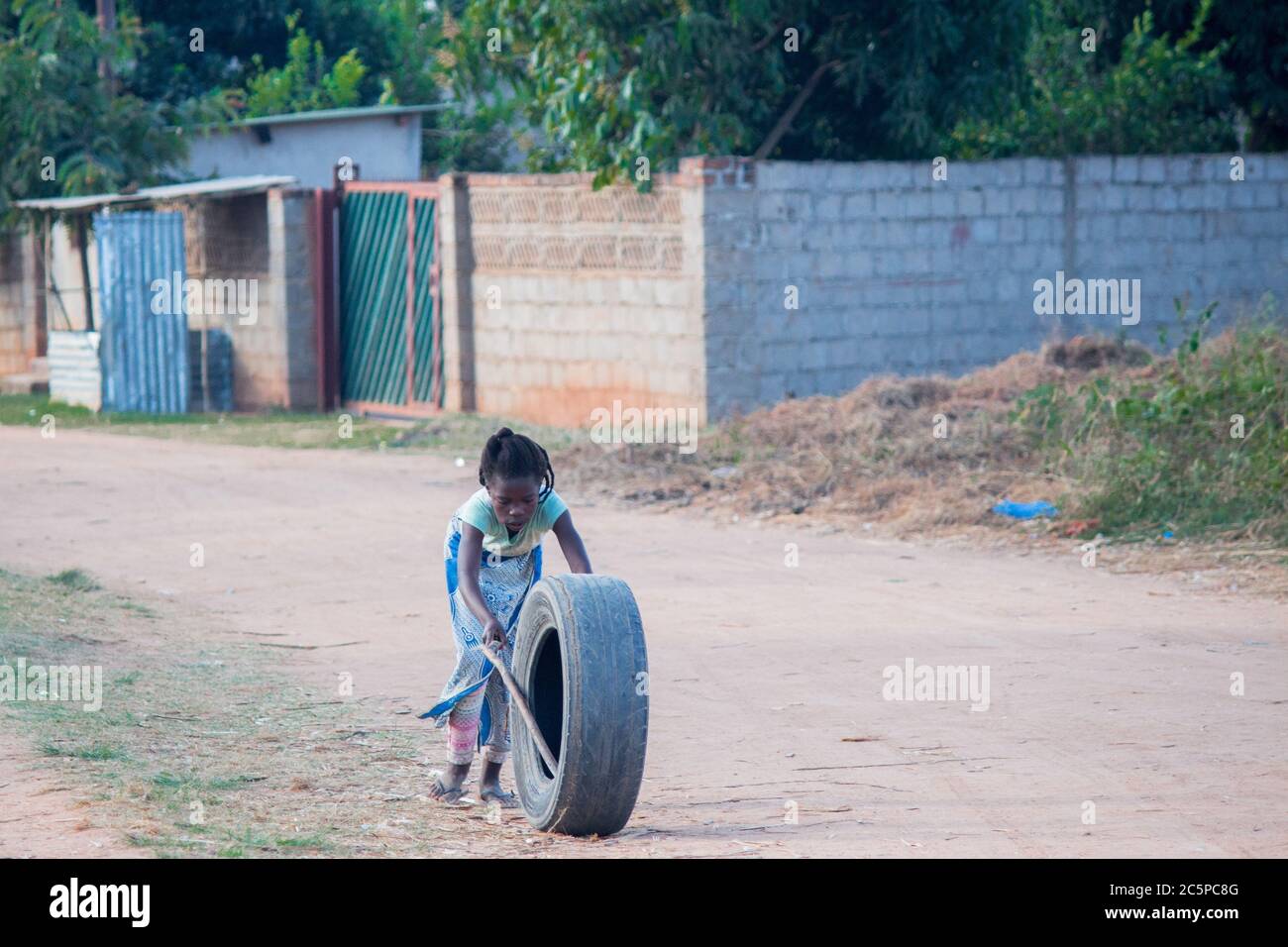 Jeune fille jouant à l'extérieur avec un jouet de pneu de voiture recyclé avec deux bâtons d'arbre Banque D'Images