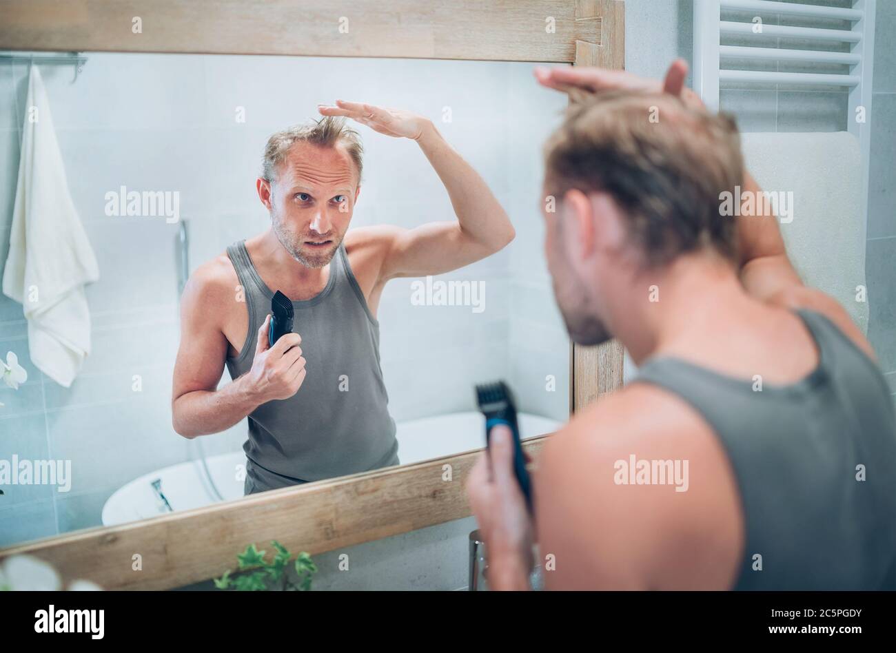 Homme regardant le miroir de salle de bain et pensant à son nouveau style coupe de cheveux analysant les cheveux tenant la tondeuse électrique rechargeable. Décision radicale, vie- Banque D'Images