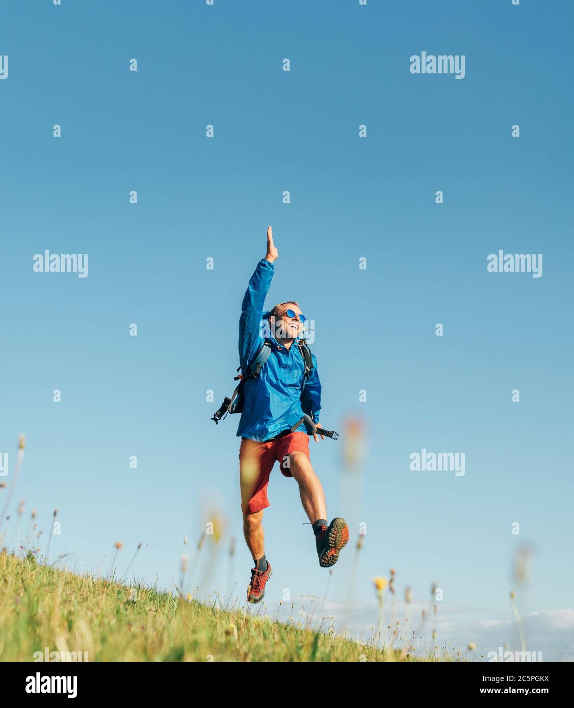 Backpacker voyageur saut émotionnellement sur l'herbe verte montagne prairie avec sac à dos avec les bras et les jambes ouverts larges. La liberté de l'homme dans la nature conce Banque D'Images