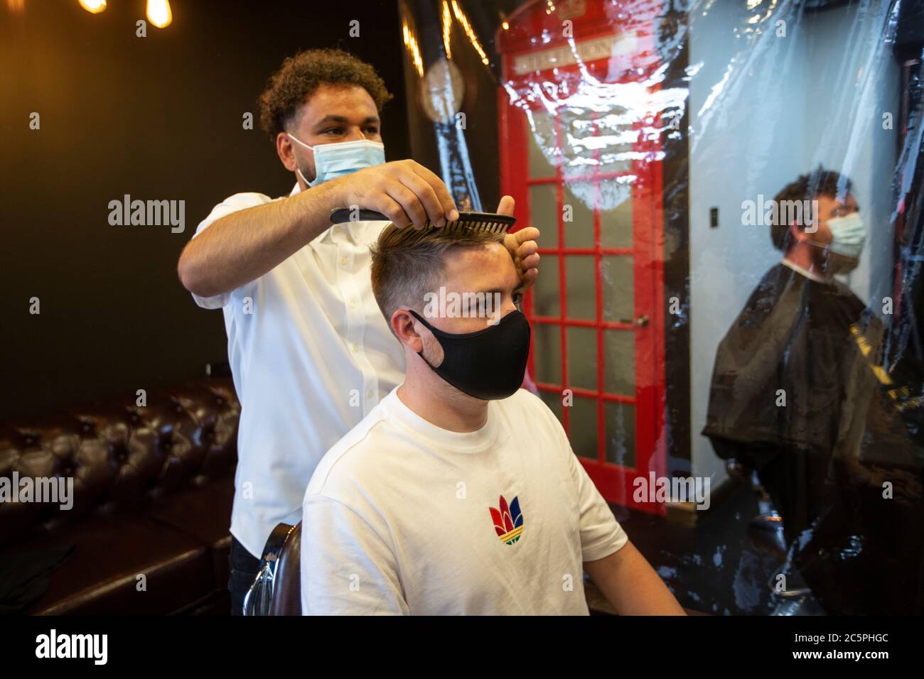 Le salon de coiffure Gentleman a rouvert avec une couverture plastique de précaution et le styliste portant des masques après les restrictions de verrouillage du coronavirus. Banque D'Images
