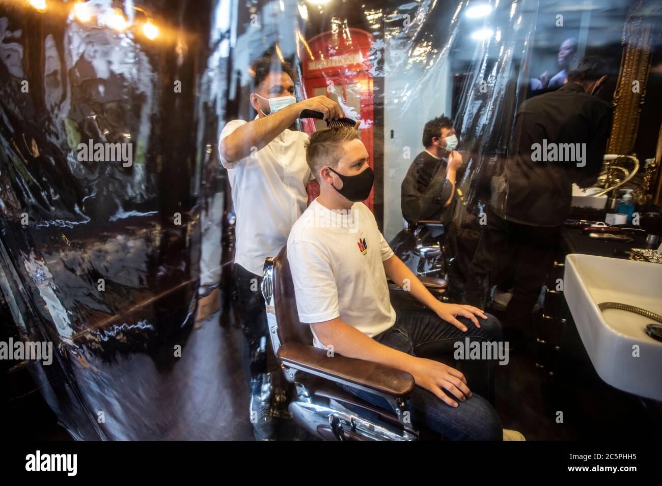 Le salon de coiffure Gentleman a rouvert avec une couverture plastique de précaution et le styliste portant des masques après les restrictions de verrouillage du coronavirus. Banque D'Images
