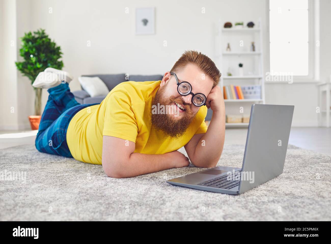 Travailler en ligne au bureau à domicile. Drôle homme travaille en ligne communique appel chat vidéo en utilisant l'ordinateur portable couché sur le sol à la maison. Banque D'Images
