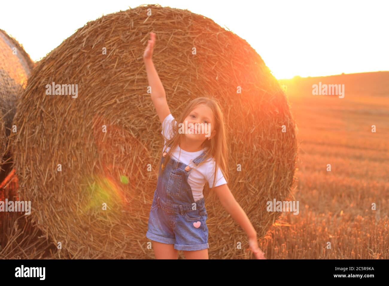 Belle petite fille se tient près d'un haystack dans un champ d'été Banque D'Images