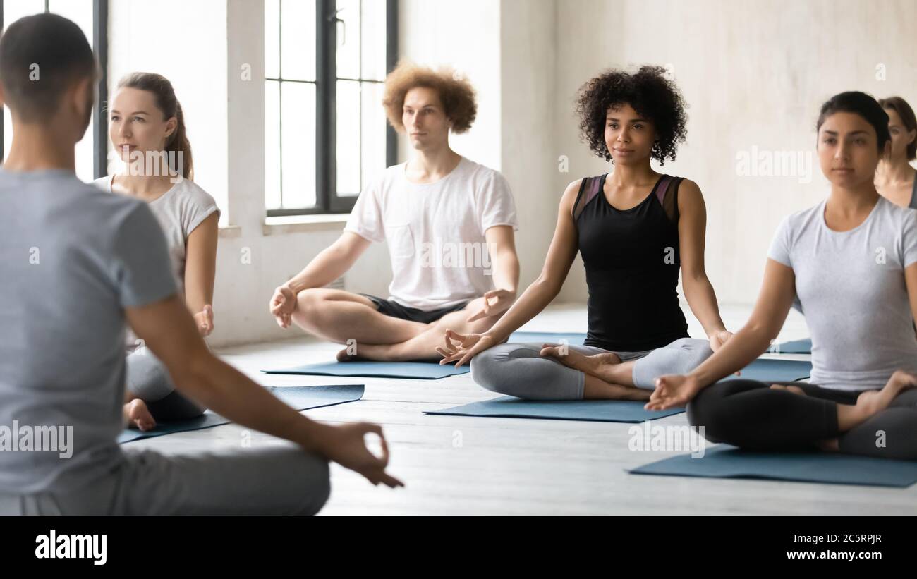 Jeunes gens de race mixte et paisibles et concentrés qui apprennent à méditer à l'intérieur. Banque D'Images