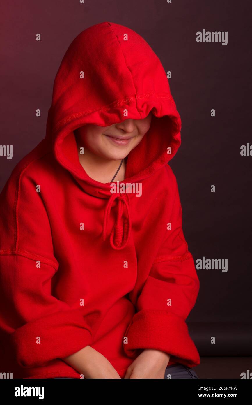 Portrait studio d'un garçon aux cheveux sombres, sur fond marron, dans une veste à capuche rouge. Émotion positive, cachez votre visage Banque D'Images
