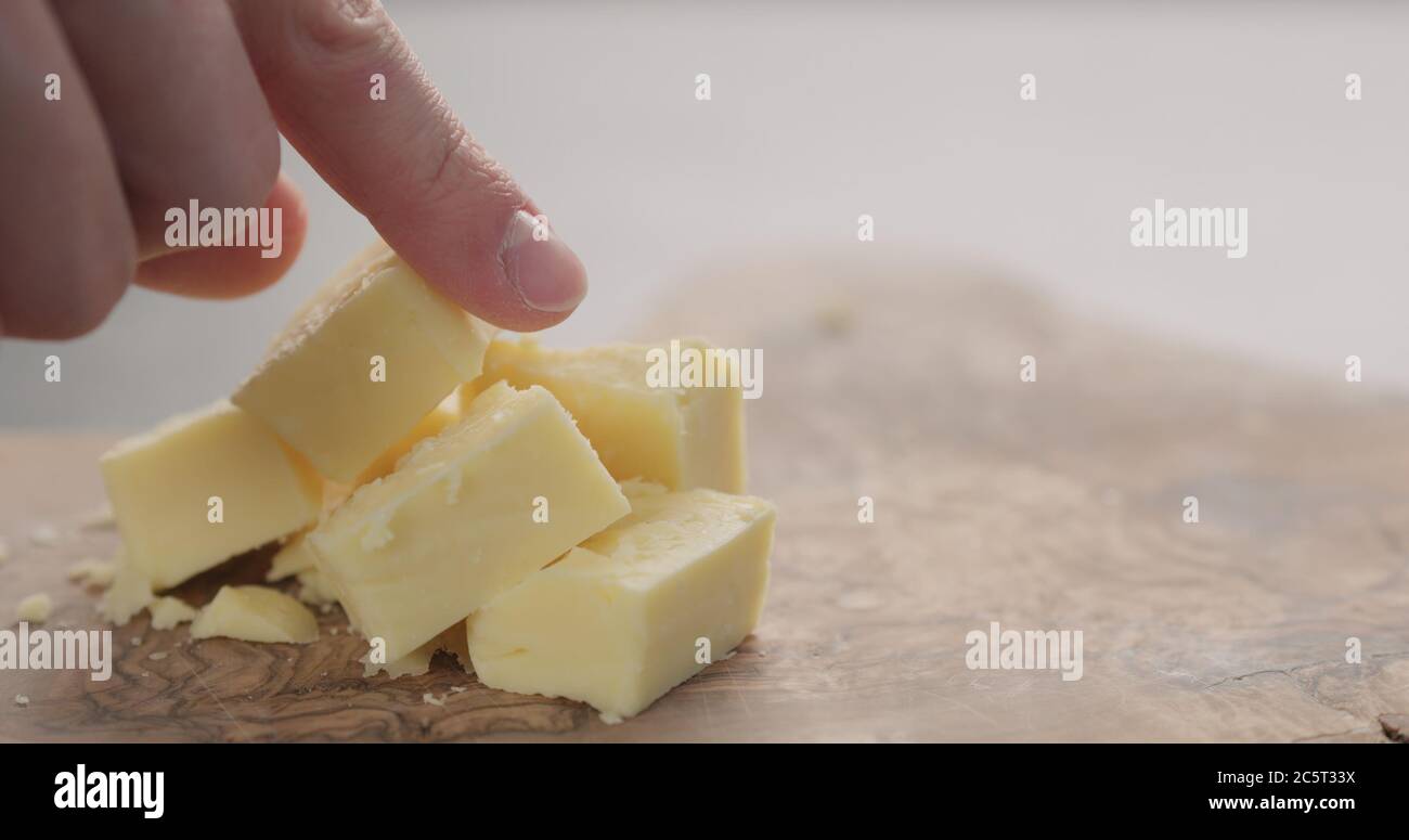 la main de l'homme prend le cube de fromage cheddar du bois d'olive gros plan Banque D'Images