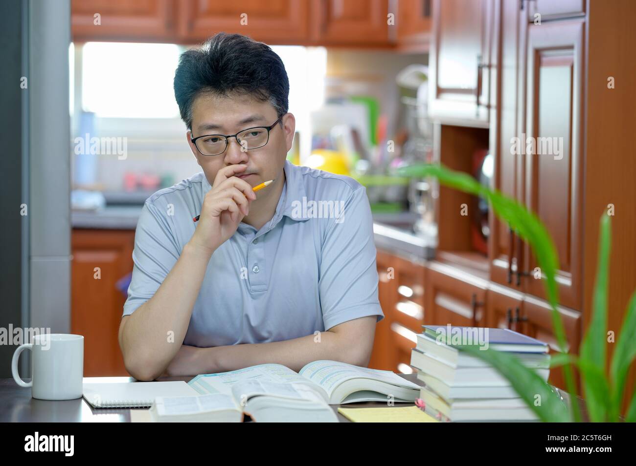 Homme asiatique d'âge moyen assis à un bureau à la maison, lisant un livre et étudiant. Banque D'Images