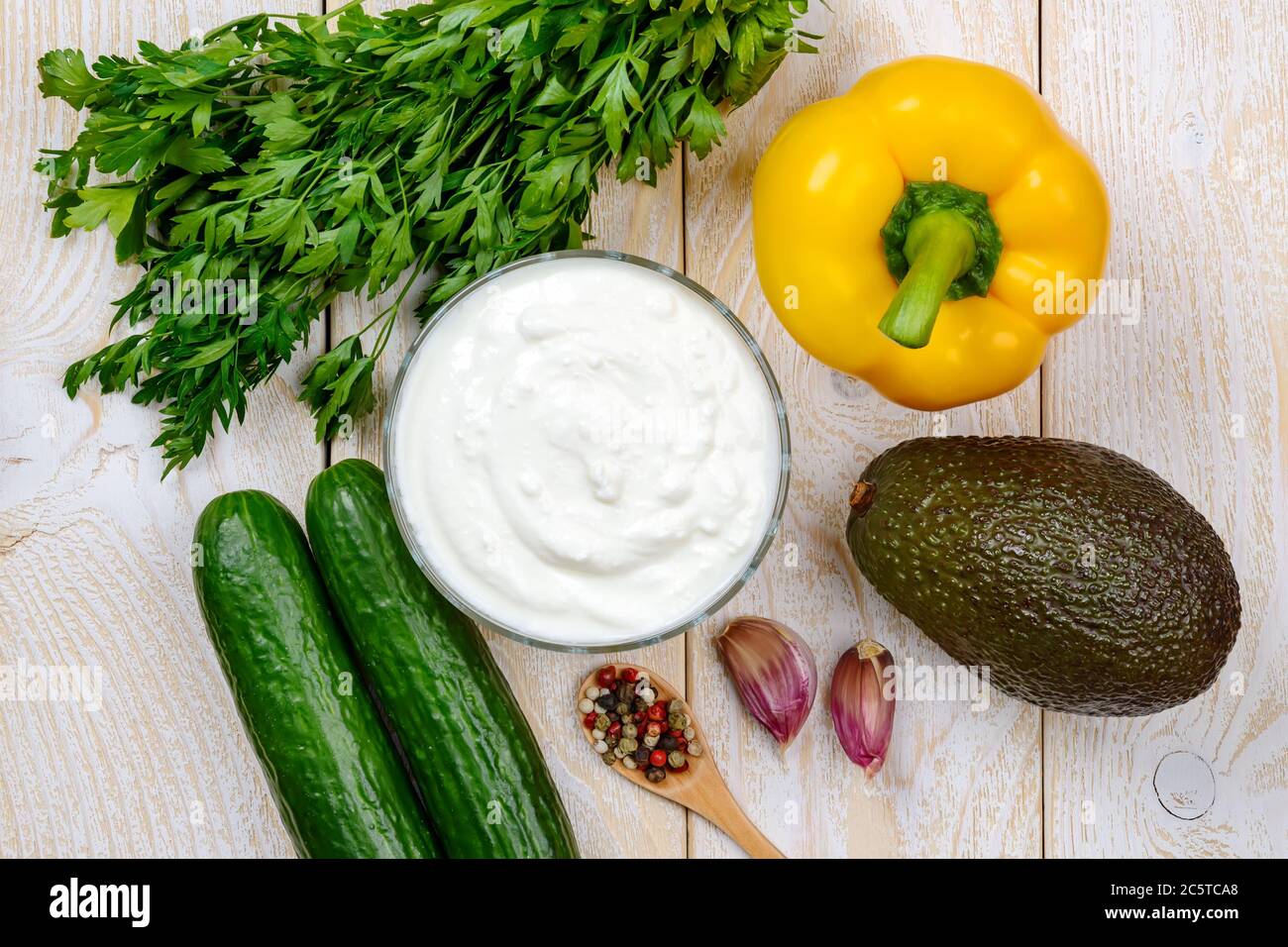 Ingrédients pour la purée de soupe de concombre crue : yaourt grec, concombre, avocat, poivron jaune, persil et ail sur une table en bois. Régime alimentaire cru. Banque D'Images