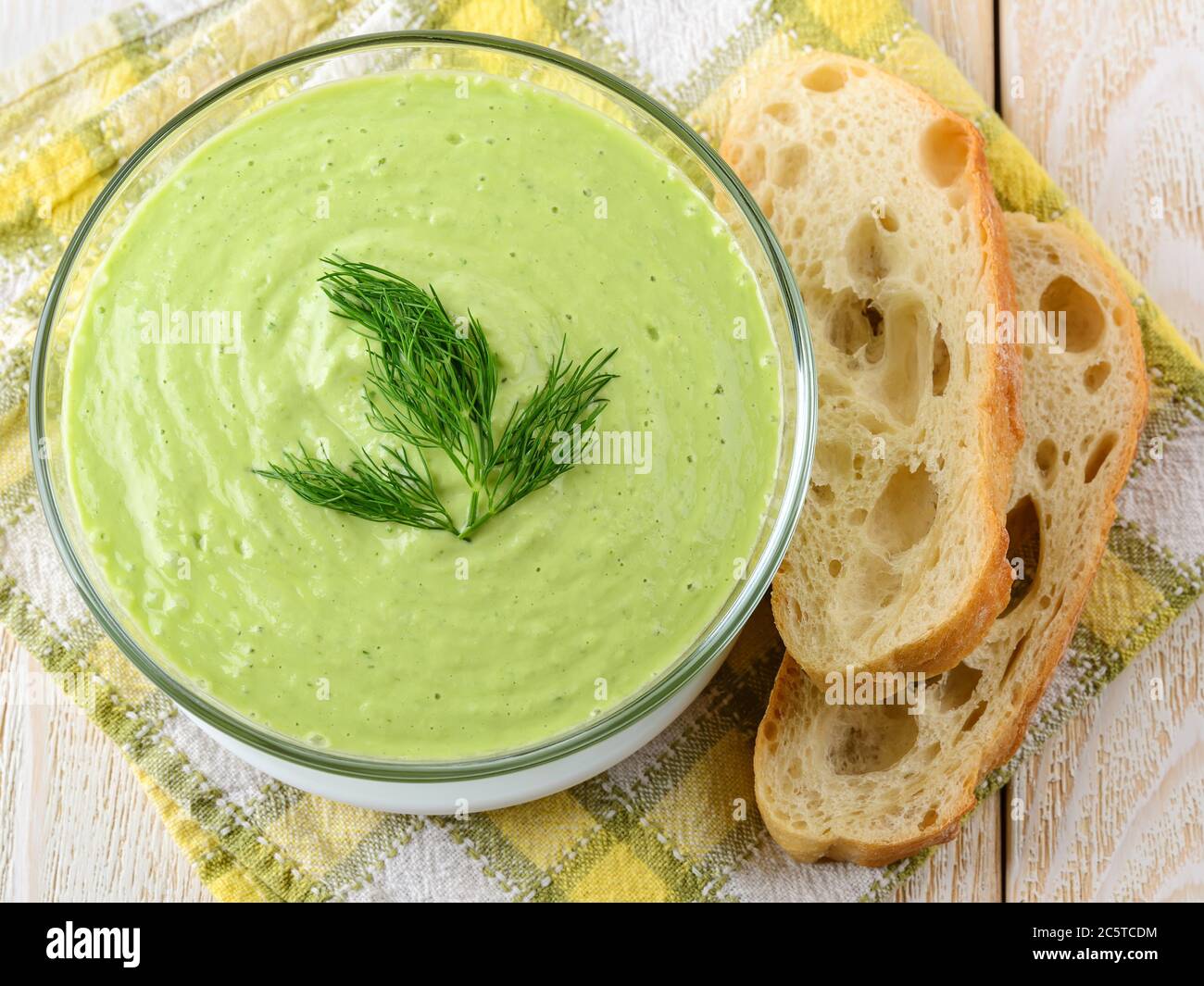 Purée de concombre frais dans un bol en verre et pain sur une table en bois blanc. Soupe de nourriture crue de yaourt grec, concombre, avocat, poivron. Banque D'Images