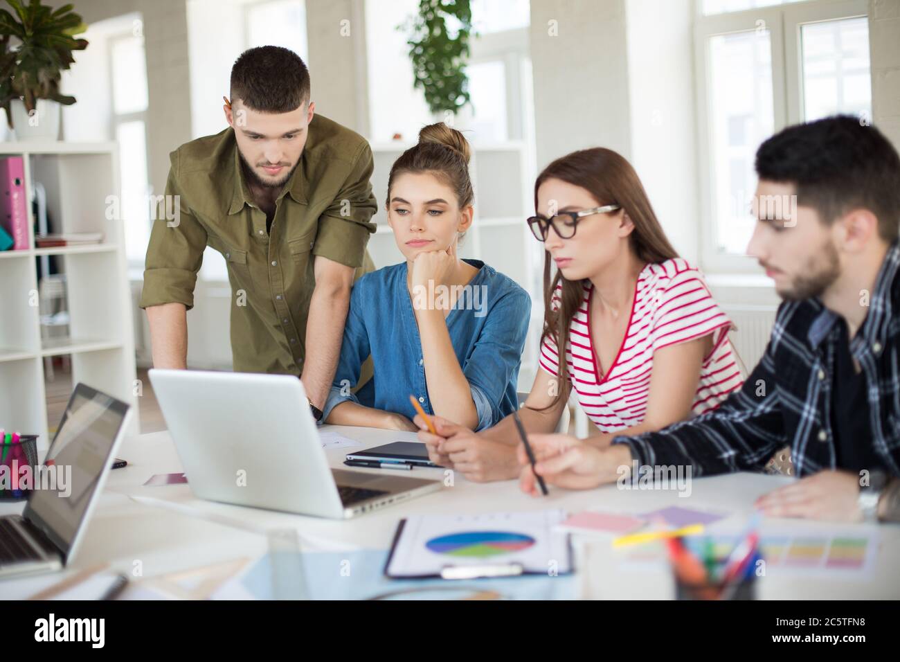 Les jeunes gens d'affaires travaillent ensemble avec soin sur un ordinateur portable. Groupe d'hommes et de femmes pensifs qui passent du temps au travail au bureau Banque D'Images