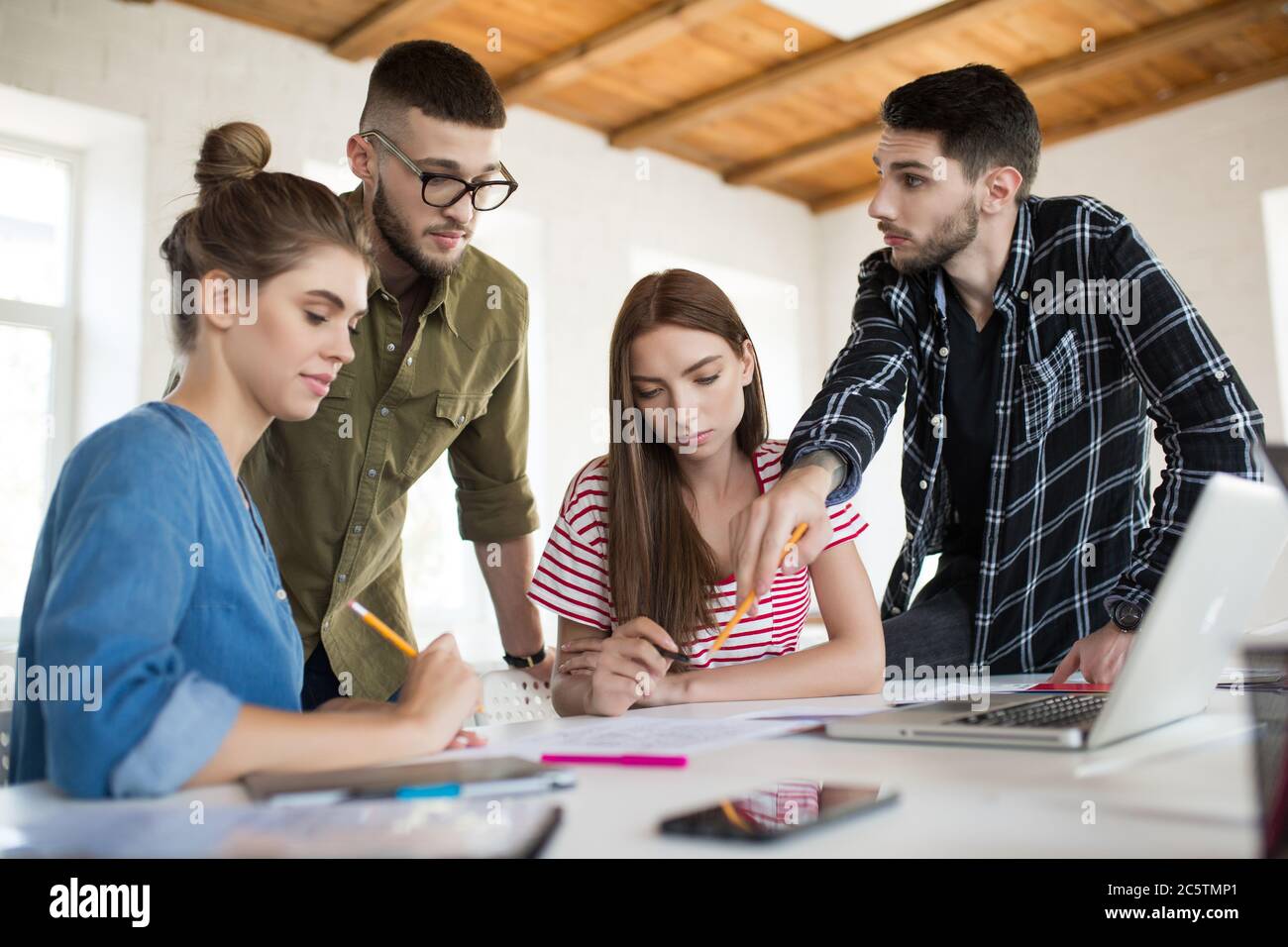 Groupe d'hommes et de femmes d'affaires pensifs travaillant avec des croquis tout en passant du temps au travail. Les jeunes créent ensemble et intelligemment un nouveau projet Banque D'Images