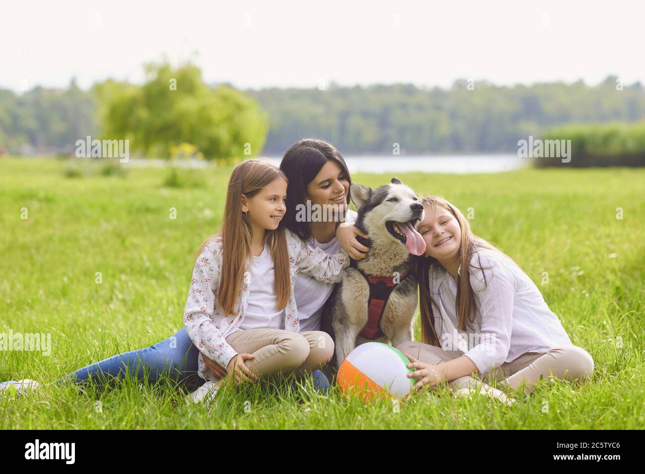 Fille mère et chien husky assis en gros plan sur l'herbe souriant heureux au week-end dans le parc d'été. Banque D'Images