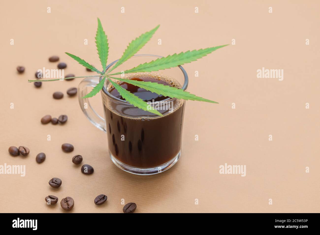 Tasse de café avec feuille de cannabis et haricots rôtis sur fond beige neutre avec espace pour le texte Banque D'Images