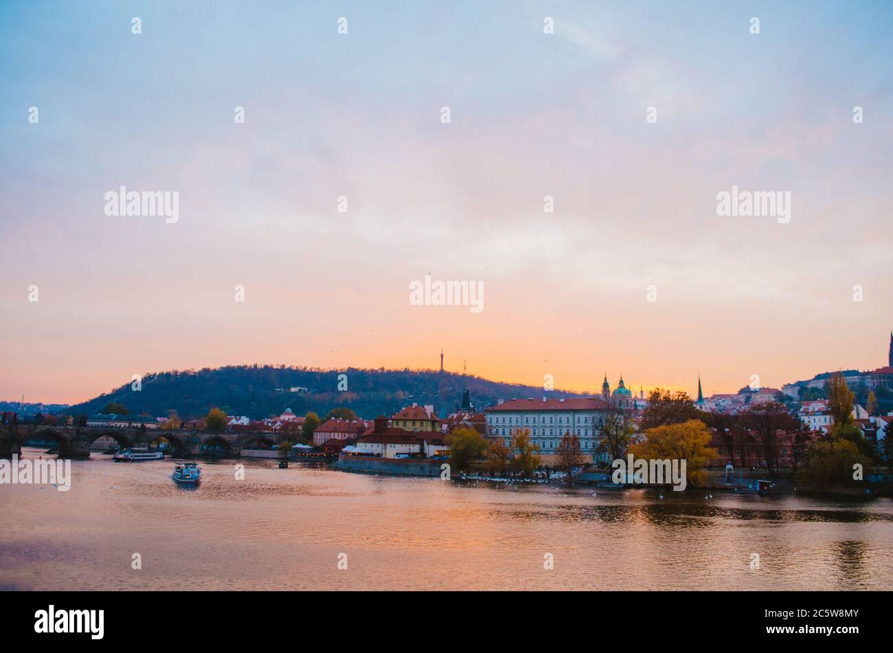 Coucher de soleil spectaculaire sur la Vltava avec un bateau passant et un dégradé de couleurs orange à rose réfléchissant du ciel dans l'eau. Banque D'Images