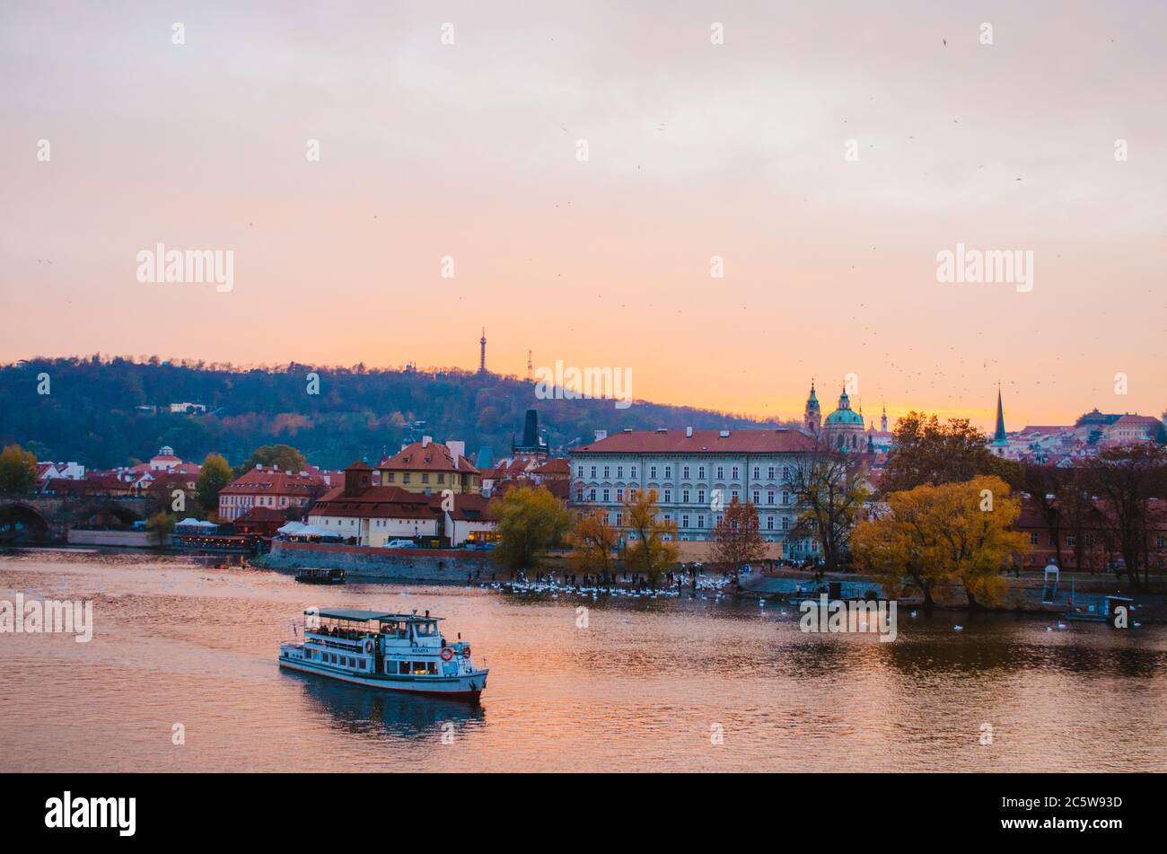 Coucher de soleil spectaculaire sur la Vltava avec un bateau passant et un dégradé de couleurs orange à rose réfléchissant du ciel dans l'eau. Banque D'Images