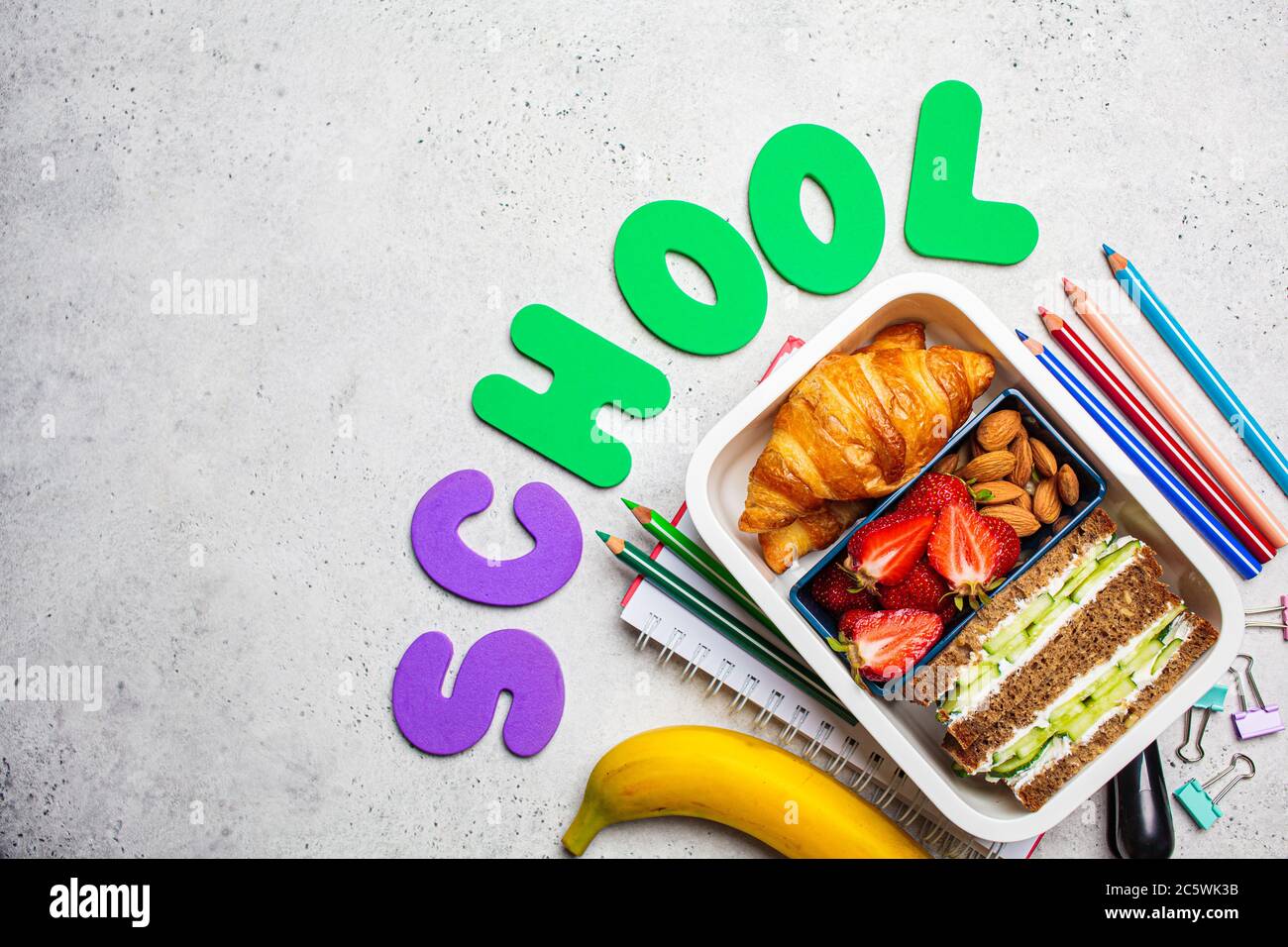 Concept de retour à l'école. Boîte à lunch avec sandwich, croissants et en-cas pour l'école. Fond de l'école avec l'inscription - école. Banque D'Images