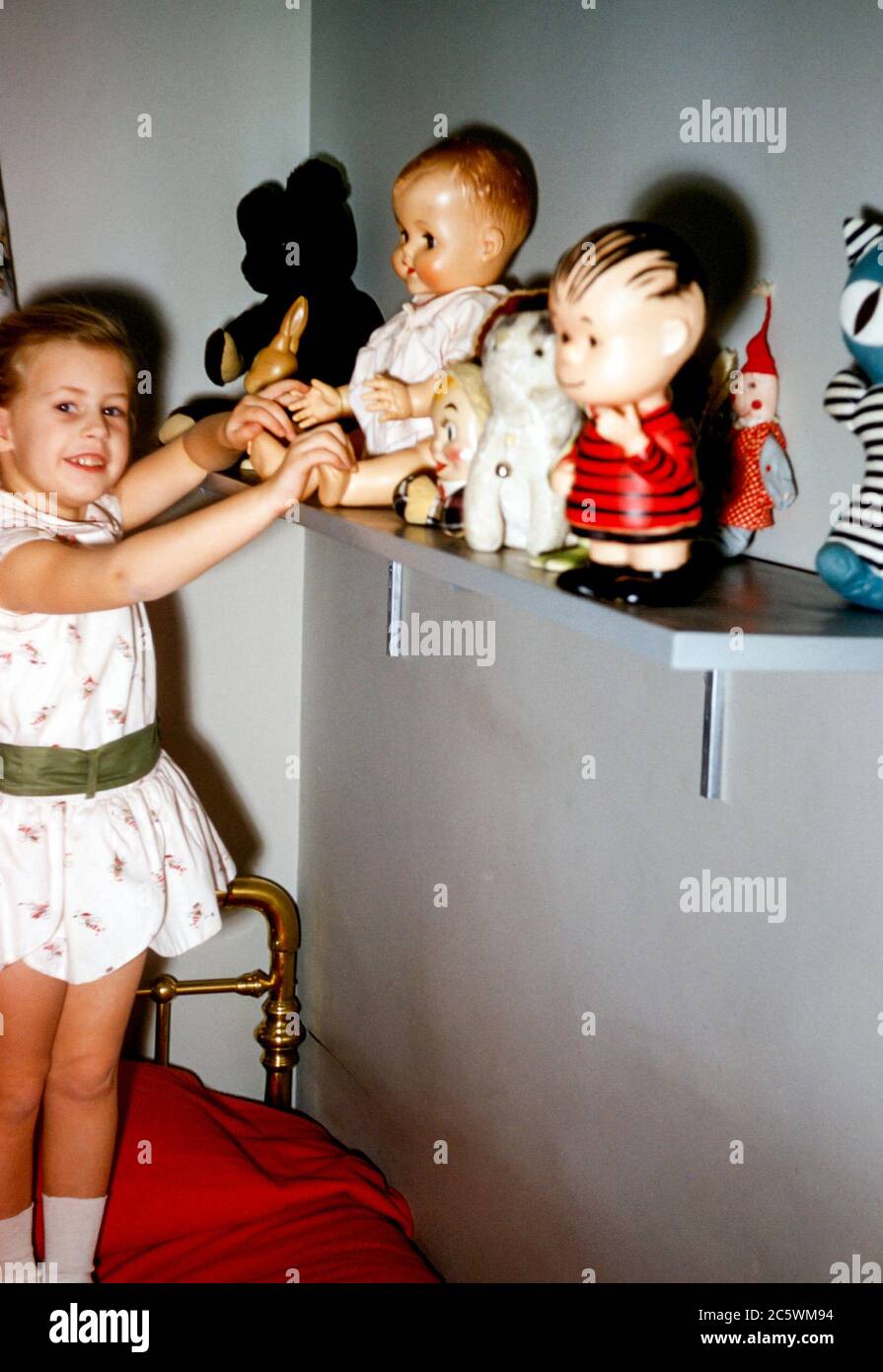 Jeune fille de 4 ans dans la chambre de l'enfant avec du laiton Lit  montrant sa collection de poupées-jouets, y compris le personnage de Linus  De Peanuts dessin animé aux Etats-Unis dans