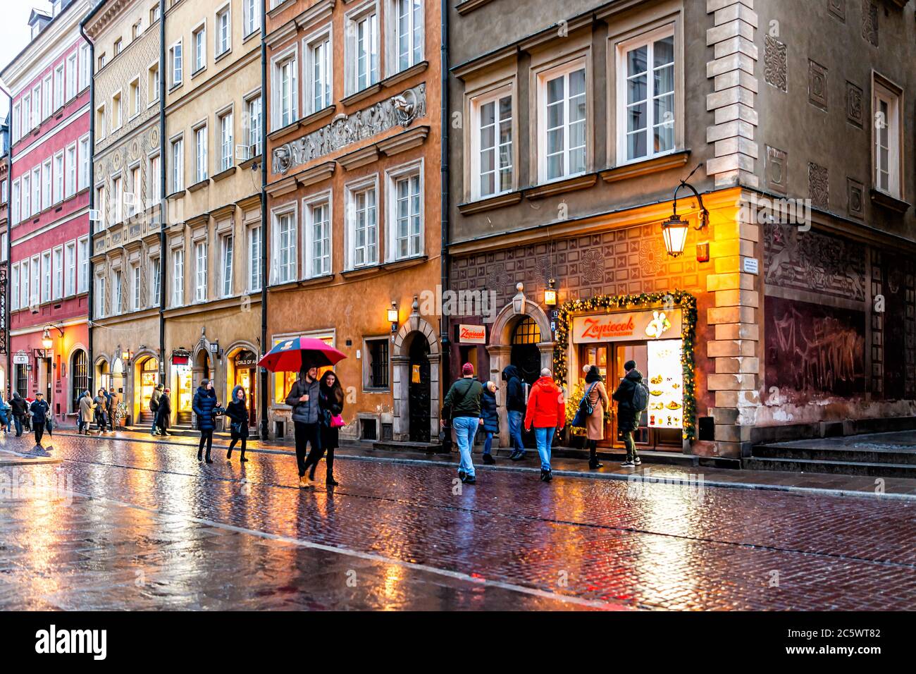 Varsovie, Pologne - 22 décembre 2019: Touristes gens marchant avec des parasols shopping à la vieille ville de Varsovie en soirée pluie pendant la réflexion d'hiver sur p Banque D'Images