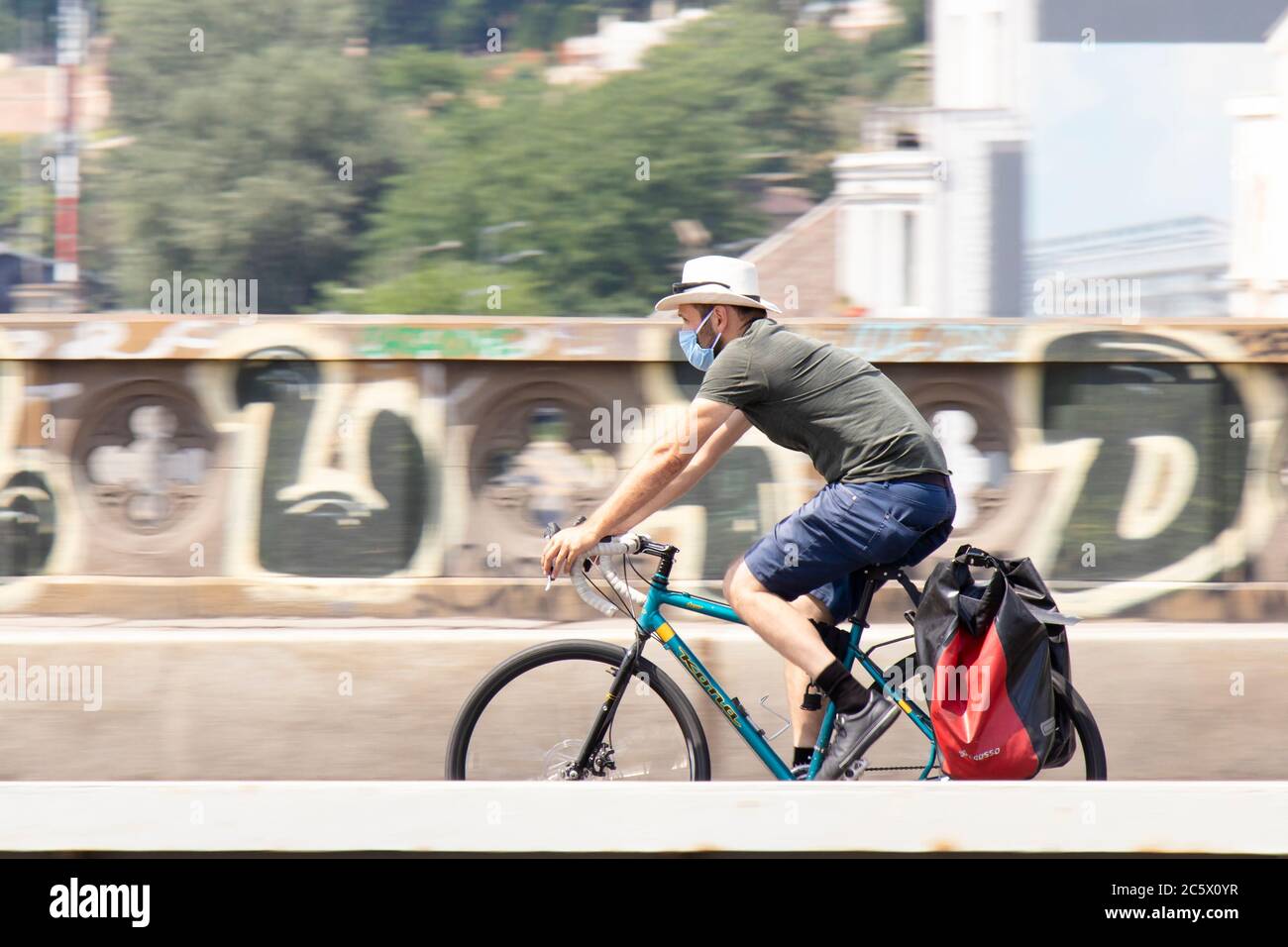 Belgrade, Serbie - 4 juillet 2020 : un jeune homme beau portant un chapeau de paille et un masque chirurgical à vélo sur le pont de rue de la ville Banque D'Images