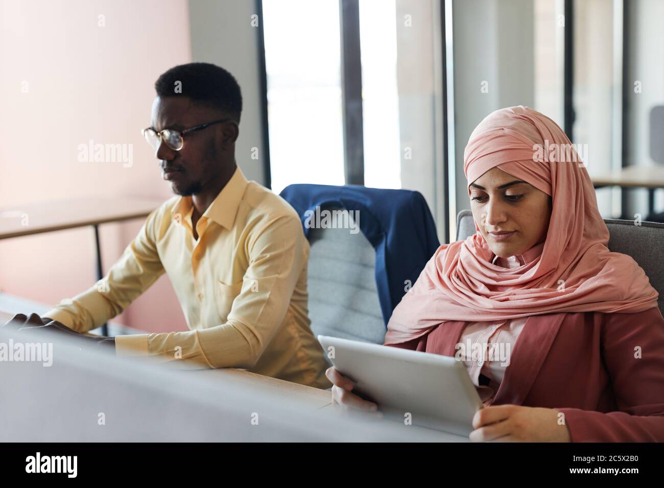 Portrait d'une jeune femme d'affaires musulmane utilisant une tablette numérique tout en travaillant au bureau avec un homme afro-américain, espace de copie Banque D'Images