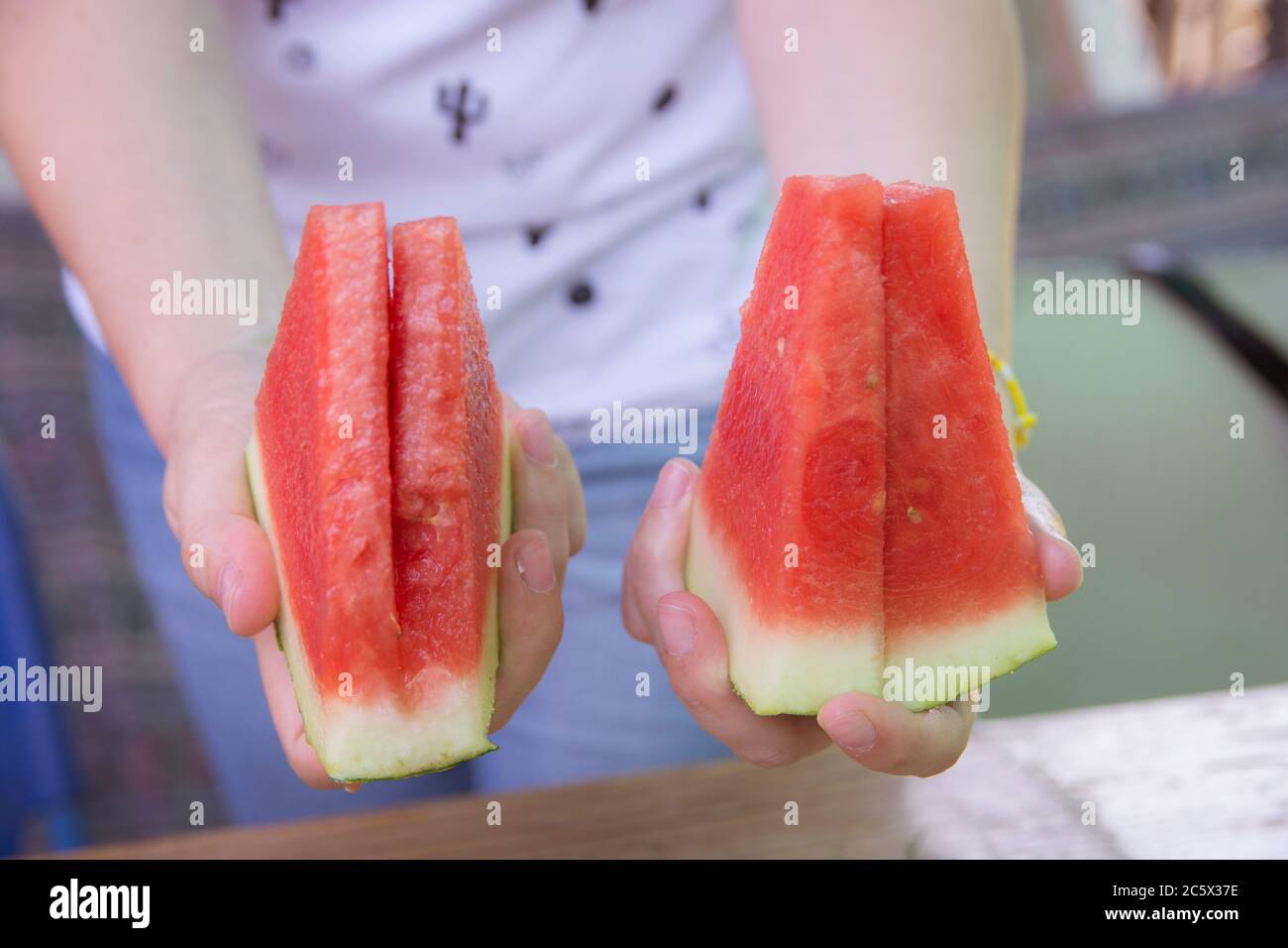 Femme tenant des tranches de pastèque fraîche (Citrullus lanatus) des deux mains. Banque D'Images
