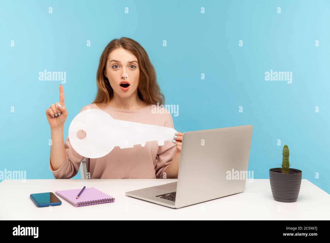 Une femme intelligente, qui s'est assise sur son lieu de travail avec un ordinateur portable, tient la clé et pointe le doigt vers le haut avec une idée de génie, une solution intelligente, a trouvé passwo Banque D'Images