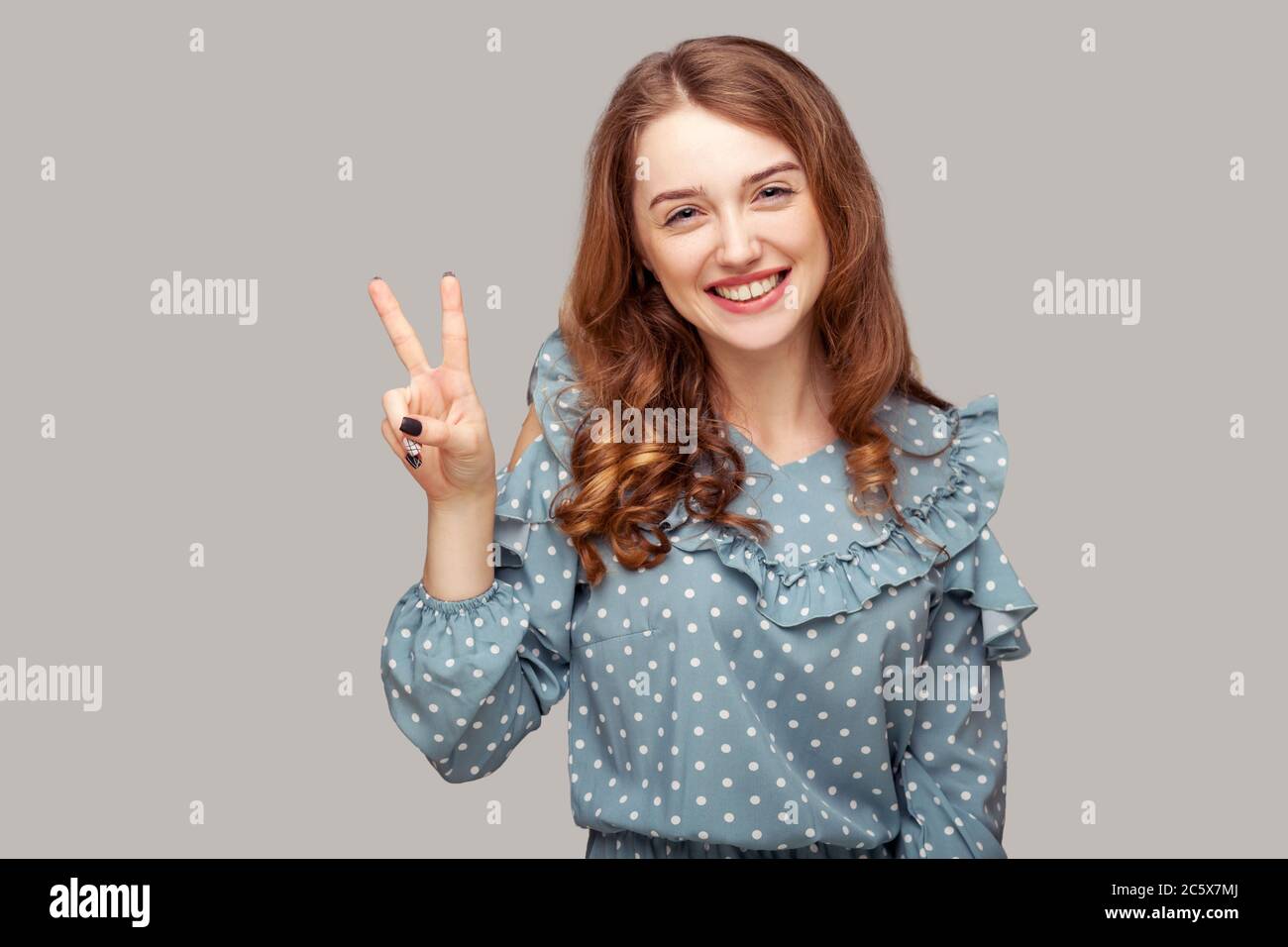 Optimiste heureux joyeuse fille blouse de volant montrant la victoire de paix geste deux doigts relevés, regardant l'appareil photo avec le sourire Toothy, appréciant la victoire de gain Banque D'Images