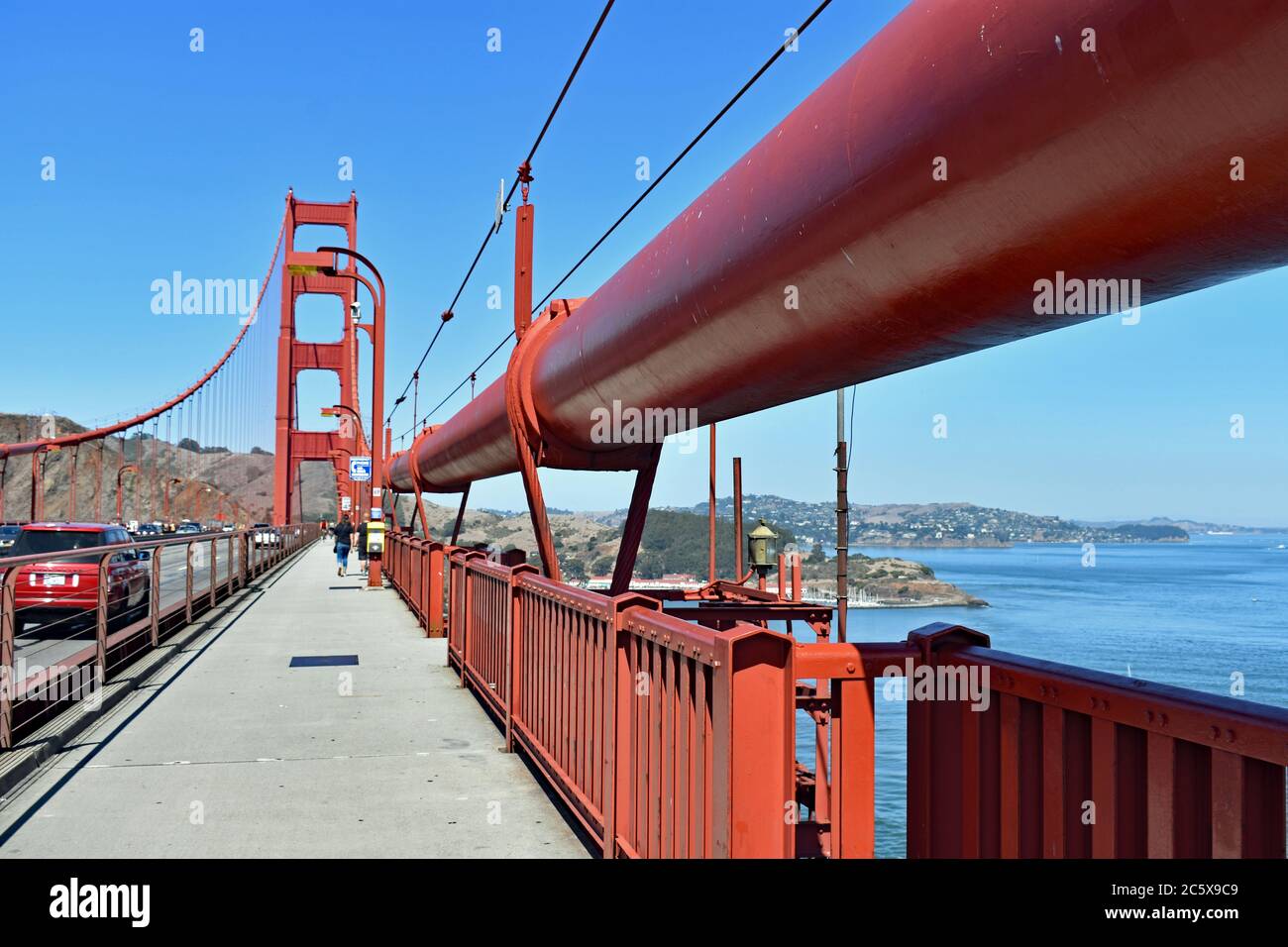 Sur le Golden Gate Bridge en suivant la ligne de suspension vers la tour nord. Une voiture rouge passant par et les Marin Headlands derrière. San Francisco. Banque D'Images