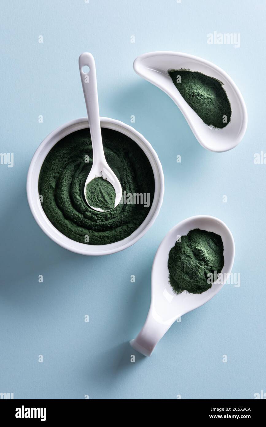 Poudre de chlorelle ou de spiruline verte dans trois bols en porcelaine blanche de forme différente et dans une petite cuillère sur fond bleu. Alimentation saine de superaliments Banque D'Images