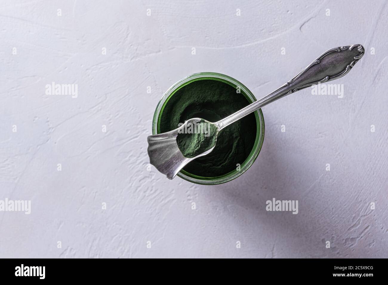 Poudre de chlorelle ou de spiruline verte naturelle dans un pot en verre rond et dans une cuillère en argent sur le bol. Concept de nourriture saine et de régime. Blanc Banque D'Images