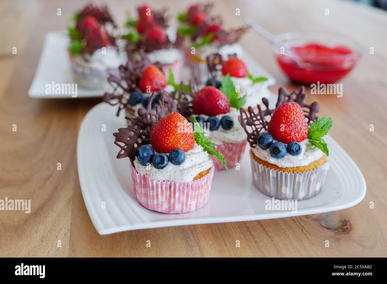 Magnifique groupe coloré de petits gâteaux décorés de crème fouettée blanche, de fraises, de bleuets, de chocolat et de menthe sur une table en bois. Banque D'Images