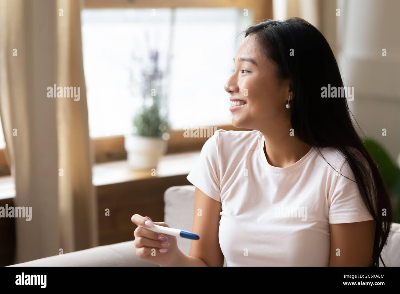 Jeune femme asiatique rêveuse qui tient un test de grossesse. Banque D'Images
