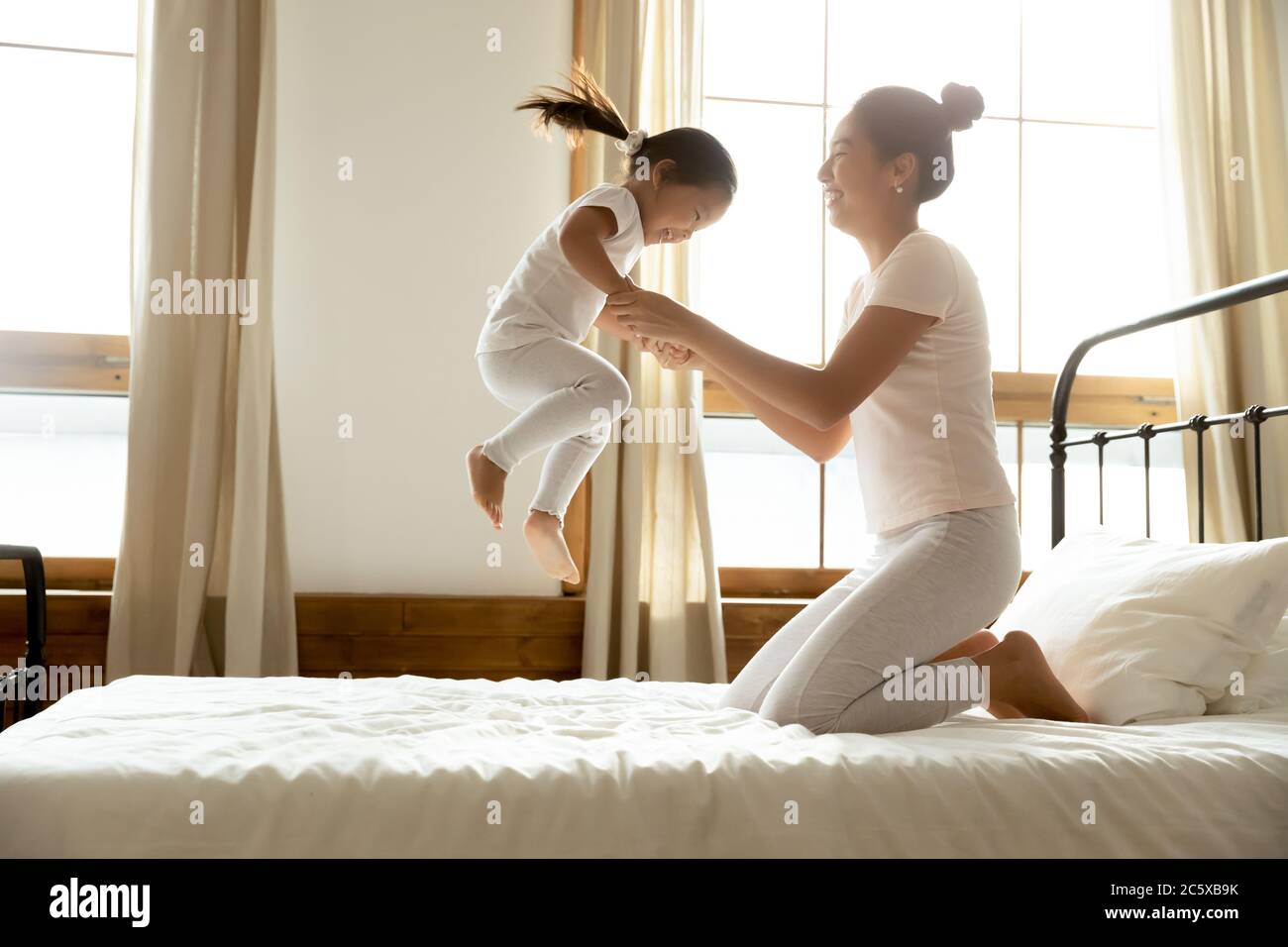 Petit Bebe Asiatique Sautant Sur Le Lit Tenant Les Mains De Maman Photo Stock Alamy