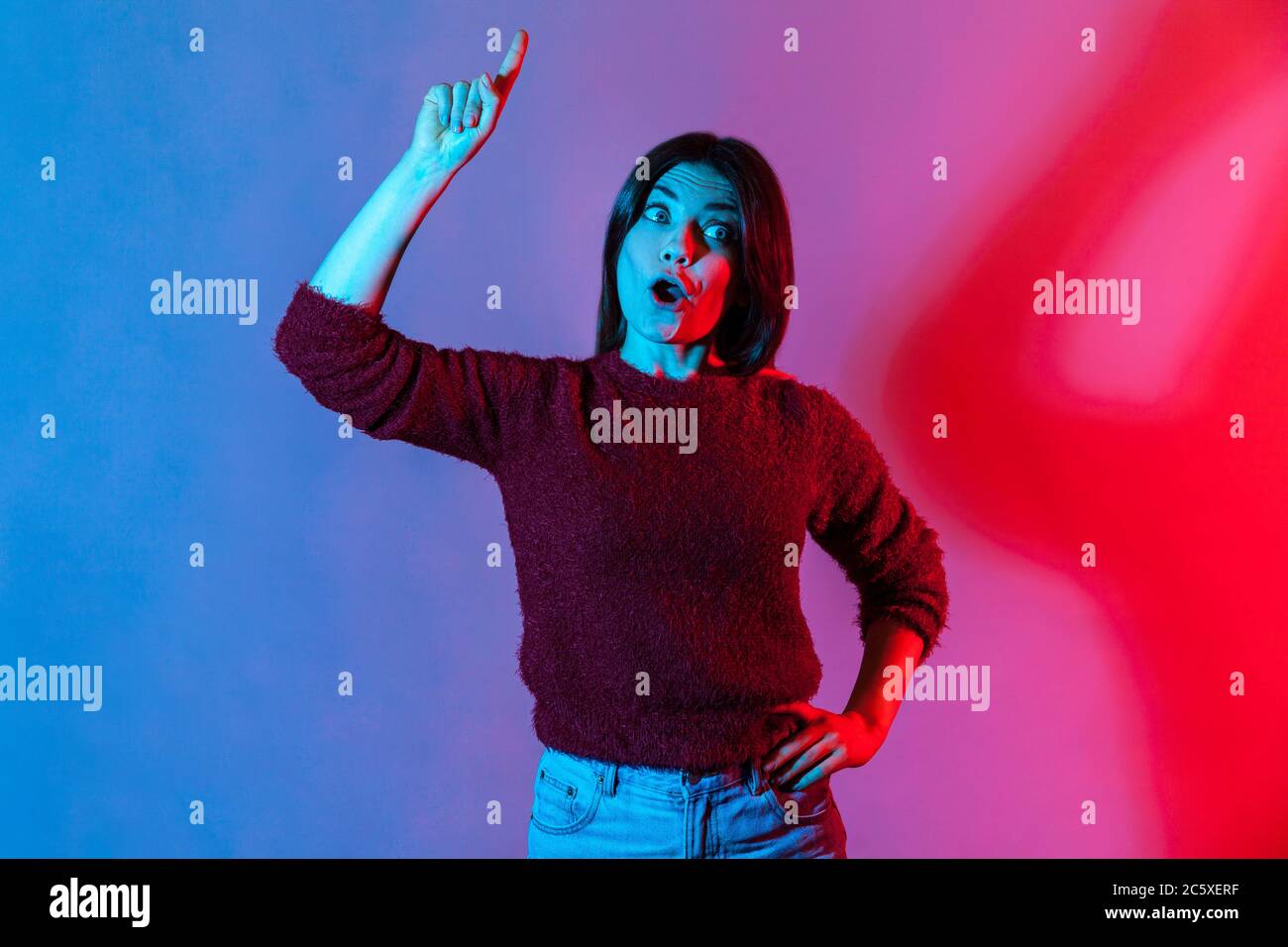 Eureka ! Portrait lumineux au néon d'une jeune fille créative inspirée pointant du doigt vers le haut avec une bonne idée et regardant stupéfait, surpris par la solution soudainement trouvé intelligente Banque D'Images