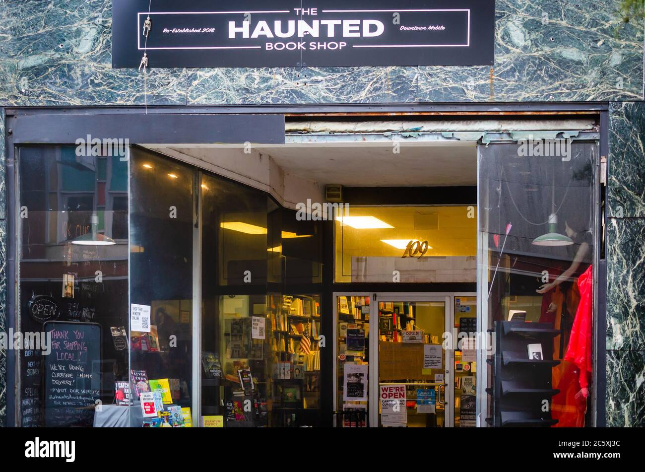 Des panneaux pour « faire des achats locaux » sont dans la fenêtre de la librairie hantée, le 3 juillet 2020, à Mobile, Alabama. Banque D'Images