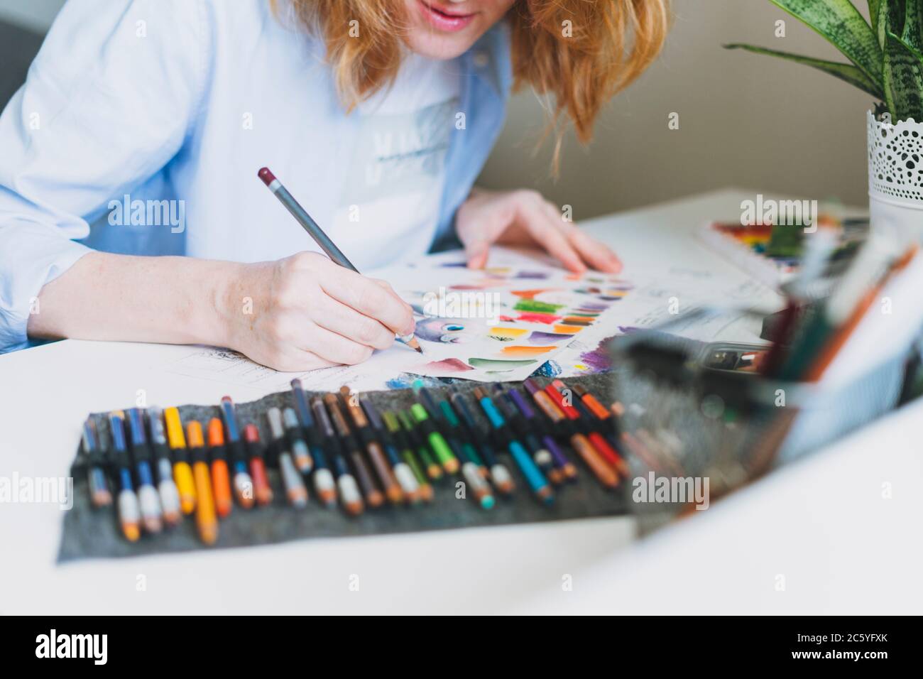 Rognez la photo de la jeune femme avec un illustrateur de cheveux rouges, l'artiste dessine à un bureau à la maison Banque D'Images
