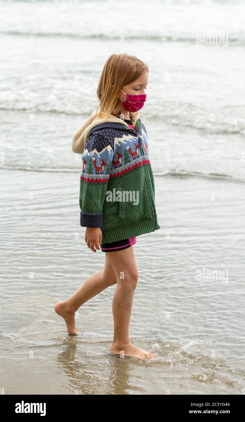 Jeune fille de six ans, dans un maillot de bain lumineux courant et jouant sur une plage de sable Banque D'Images