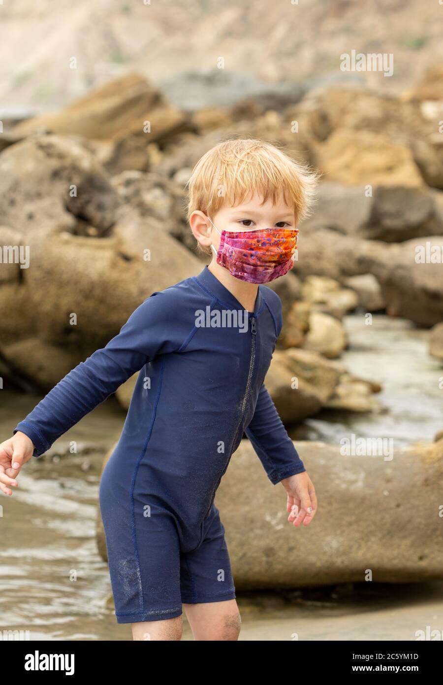 Un jeune garçon en costume de natation et un masque facial lumineux jouant dans certaines piscines de marée Banque D'Images