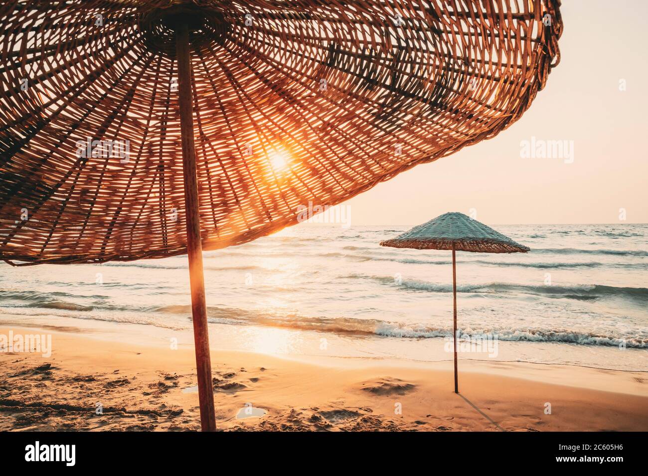 Parasol sur une plage de sable. Soleil à travers l'Osier parapluie à Lever  coucher d'été Photo Stock - Alamy