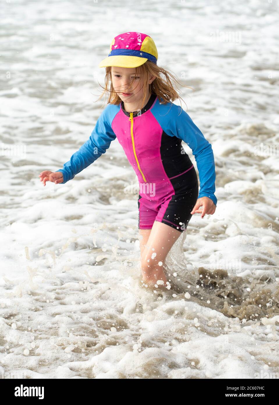 Jeune fille de six ans, dans un maillot de bain lumineux courant et jouant sur une plage de sable Banque D'Images